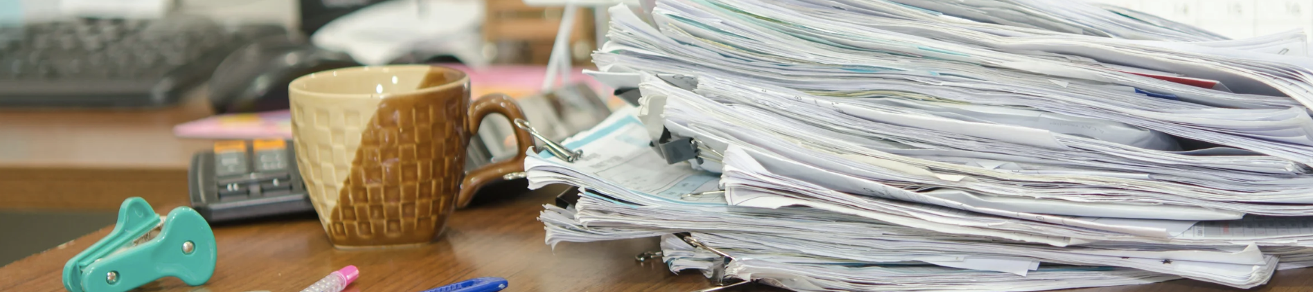 A cluttered desk with stacked papers symbolising stress, anxiety, and the feeling of being overwhelmed by everyday life.