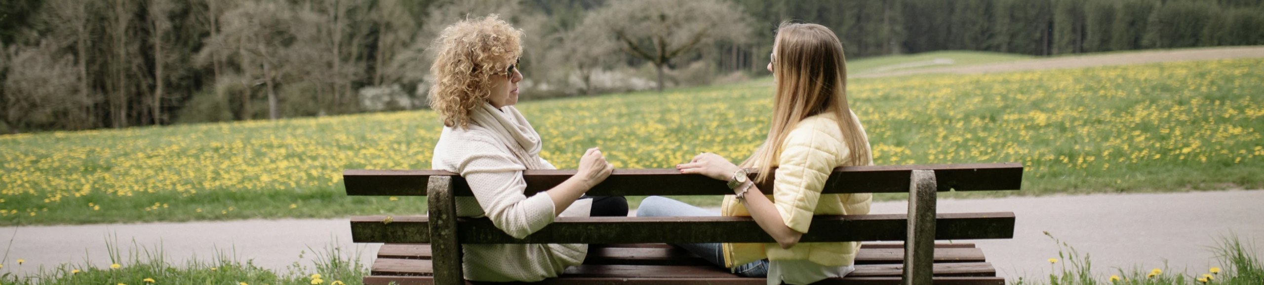 Two women sitting on a park bench talking, representing open conversation and emotional connection.
