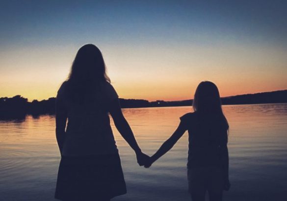 Mother and daughter holding hands, looking into the sunset over calm water, symbolising support and guidance in counselling for children and adolescents.